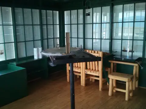 An interior view of a fire lookout cabin with a fire finder table and wooden furniture.