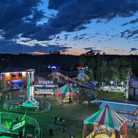 An illuminated carnival operating at twilight under a dramatic cloudy sky.