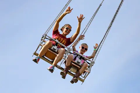 A woman and a young girl ride a swinging carnival ride with their arms raised.