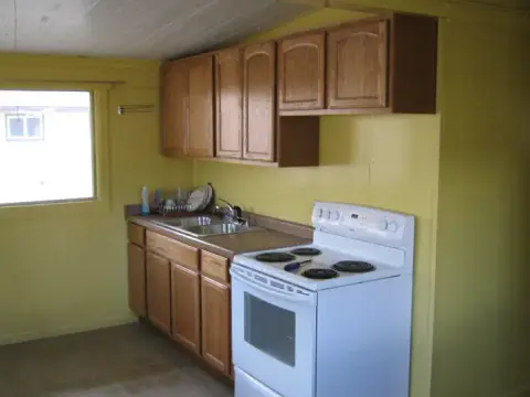 An indoor view of a simple kitchen with yellow walls and wooden cabinets.