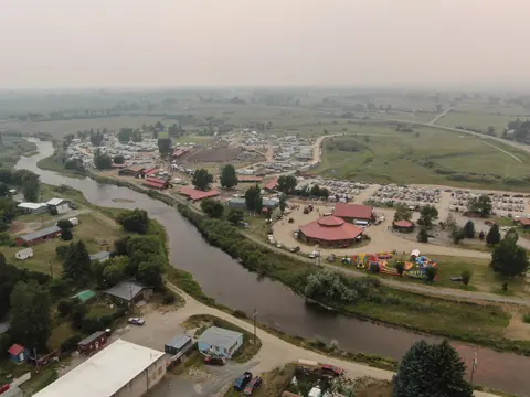 An aerial view shows a rural fairground alongside a winding river.