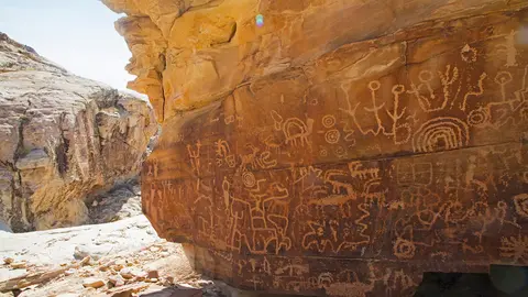 Ancient petroglyphs carved into a rock face in a desert landscape.