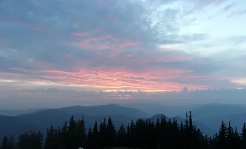 A sunset view over mountainous landscape with evergreen trees in the foreground.