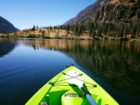 A person kayaking on a calm lake surrounded by mountains and trees.