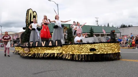 A parade float decorated in gold drives down a street with people on it.