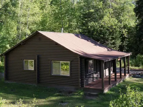 A brown wooden cabin with a metal roof and front porch nestled among trees.
