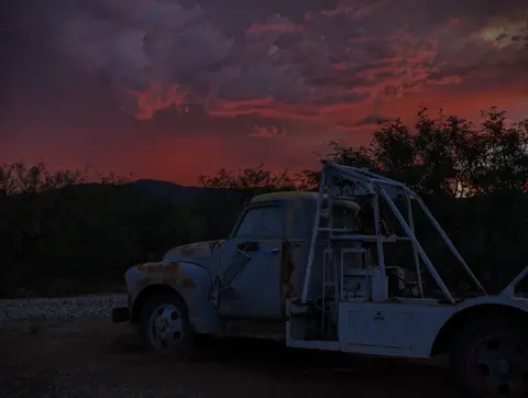 An old rusty tow truck is parked under a dramatic sunset sky.