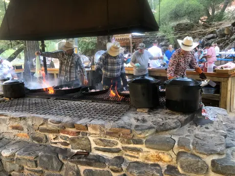 People cook food over a large stone grill outdoors.