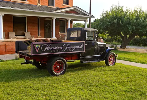 A vintage truck parked on the lawn in front of a brick house.