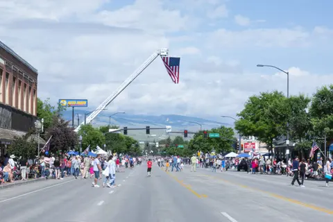 A large crowd gathers along a street for a parade with an American flag displayed from a ladder truck.