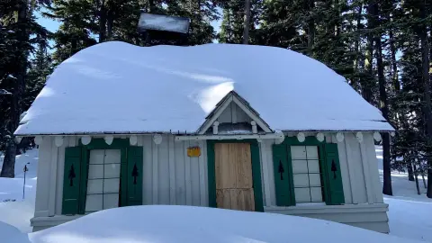 A small cabin covered in snow in a forest.