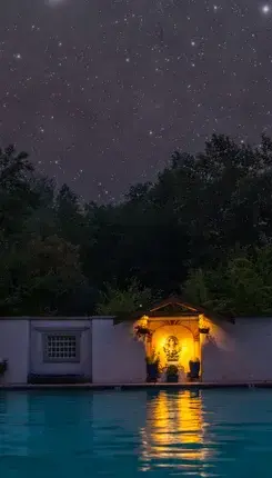 A brightly lit alcove by a swimming pool under a starry night sky.