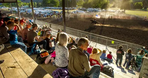 Spectators watch a rodeo event from wooden grandstands.
