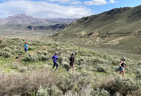 People run on a trail through a landscape of hills and mountains.
