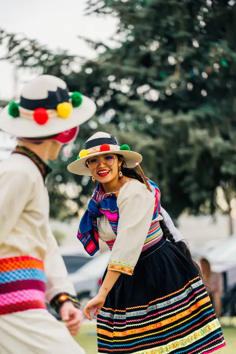 A smiling woman in traditional attire and hat dances outdoors.