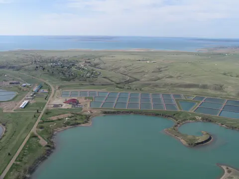An aerial view of rectangular ponds next to a large lake and rolling hills.