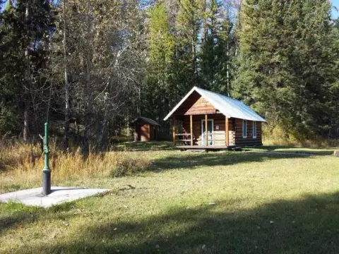 A small log cabin and water pump in a wooded area.
