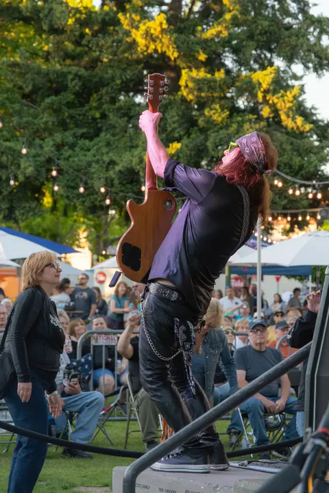 A musician holds a guitar up high while performing outdoors in front of a crowd.