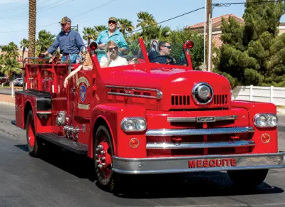 People riding in a vintage red fire truck on a sunny day.