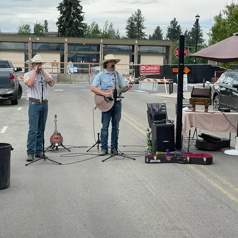 Two musicians play music outdoors on a street.