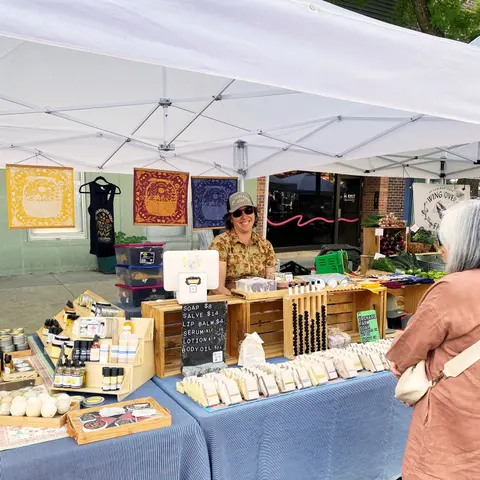 A vendor working at an outdoor market stall selling soap and other body care items.