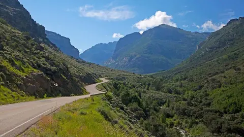 A winding road through a mountain valley under a partly cloudy sky.