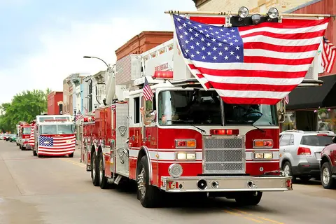 A fire truck decorated with American flags drives down a city street.