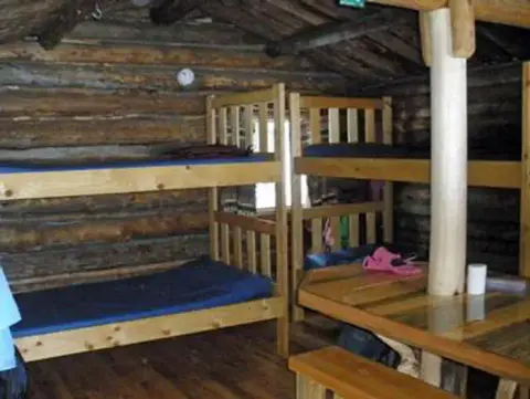 An interior view of a rustic log cabin with bunk beds and a wooden table.