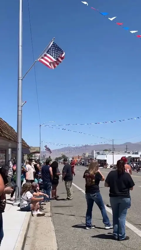 A crowd of people gathers along a street decorated with flags and bunting.
