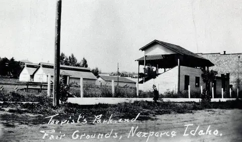 Historic black and white photograph showing a view of fairgrounds with buildings and a grandstand.