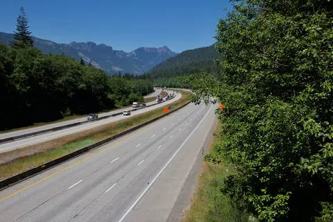A multilane highway winds through a mountain landscape under a clear blue sky.