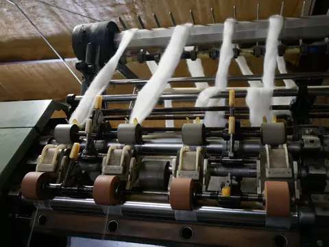 A textile machine processing white wool fibers.