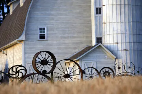 An exterior view of a rustic white barn with metal wheels arranged in front.