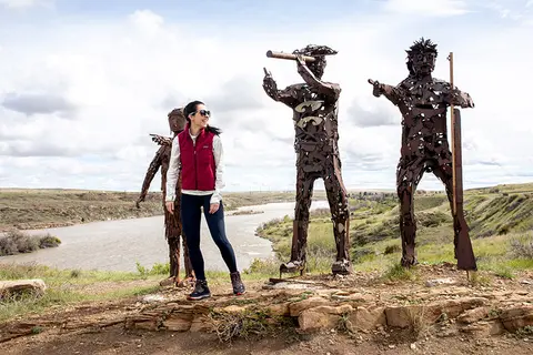 A woman stands posing near metal sculptures overlooking a river landscape.