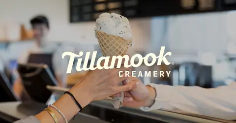 An ice cream cone being handed over a counter inside a creamery.