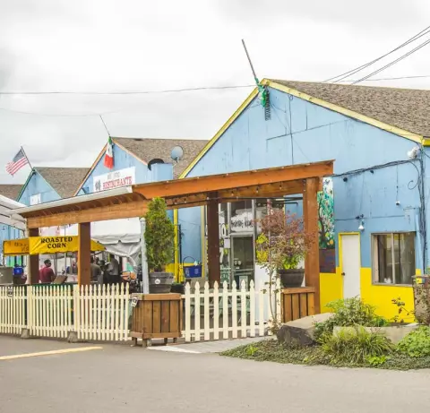 Exterior view of a blue and yellow building with a wooden pergola and white picket fence.