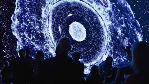 People watch a large illuminated projection of a celestial object.