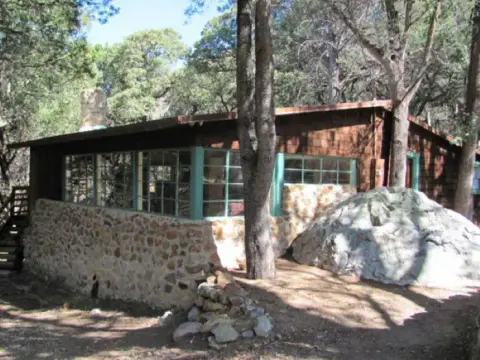 A rustic wooden cabin with a stone foundation sits among trees.