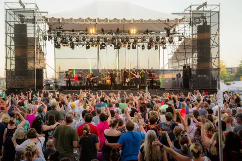 A crowd of people watches a band perform on an outdoor stage.