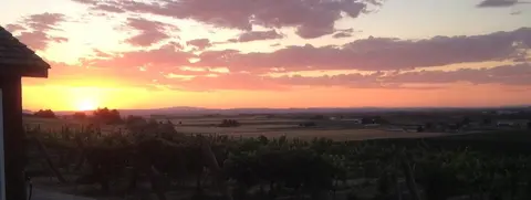 A sunset view over a rural landscape with fields and a building roof on the side.