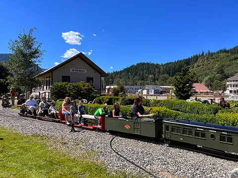 A miniature train carrying passengers on a track outdoors.