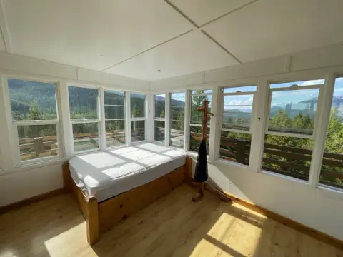 A bright room with a bed and many windows overlooking a forest and mountains.