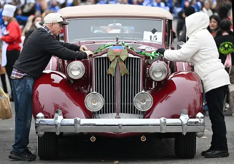 Two people decorate a classic car with festive garland and a bow.