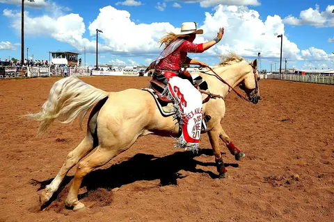 A woman riding a horse in an arena while waving.