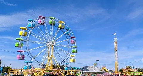 A colorful Ferris wheel and other amusement park rides under a blue sky.