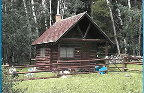 A log cabin stands in a clearing surrounded by trees.