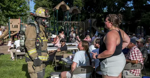 A firefighter in gear talks with people gathered outside near a playground.
