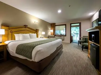 A hotel bedroom featuring a large bed with a wooden headboard and a view into a sitting area.
