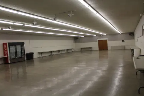 An empty function room with long tables and a vending machine.