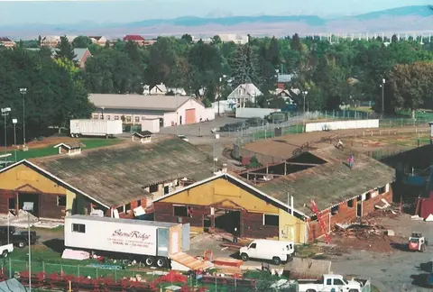An elevated view shows two wooden buildings undergoing renovation with trucks parked outside.